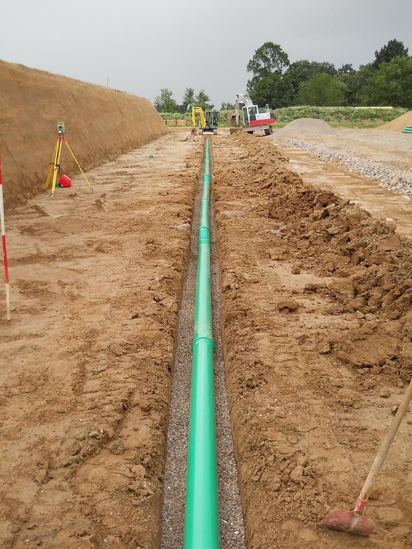 Auf einer Baustelle wird ein grünes Rohr im Dreck verlegt.