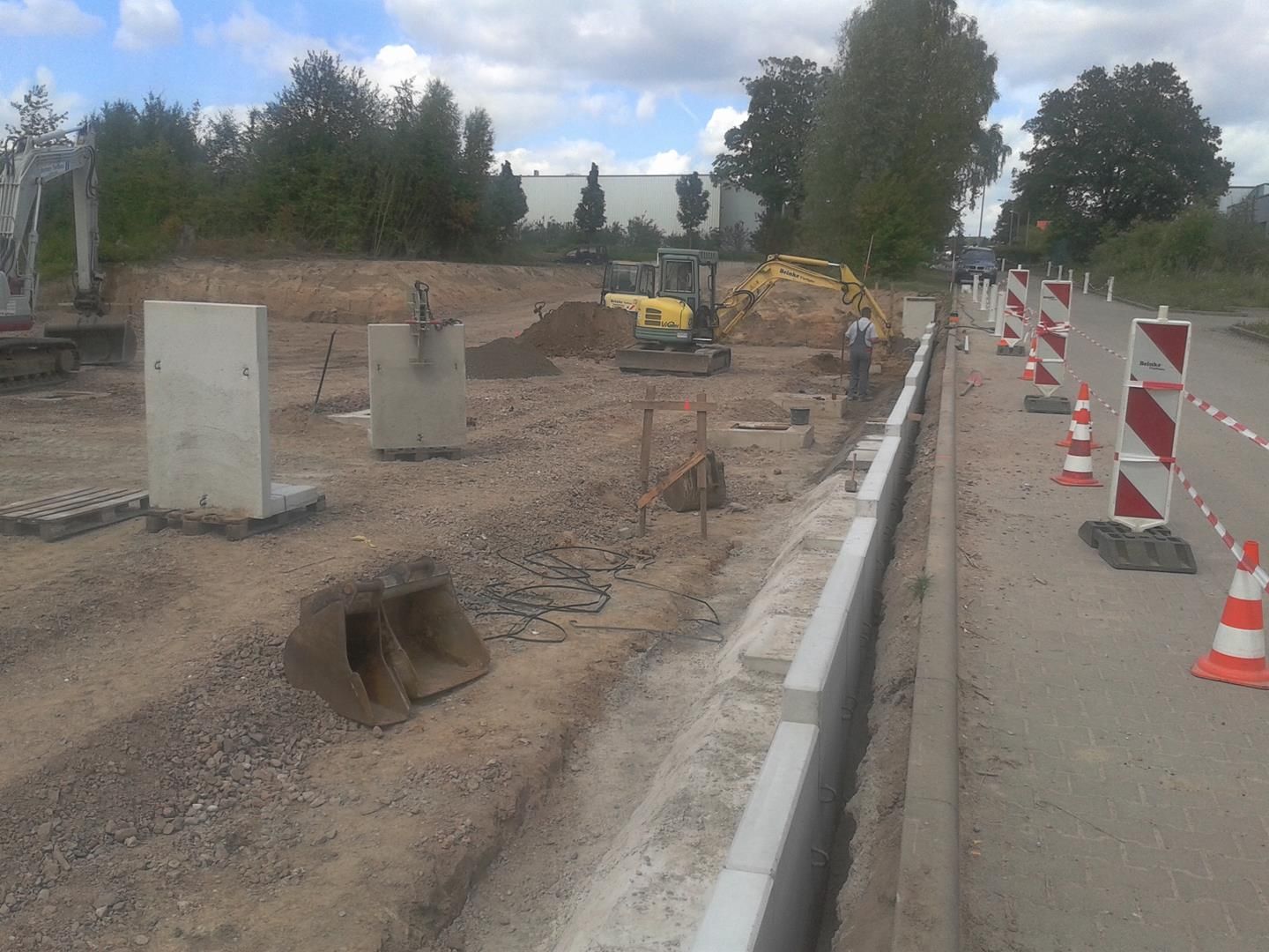 eine Baustelle mit orange-weißen Kegeln und einem gelben Bagger