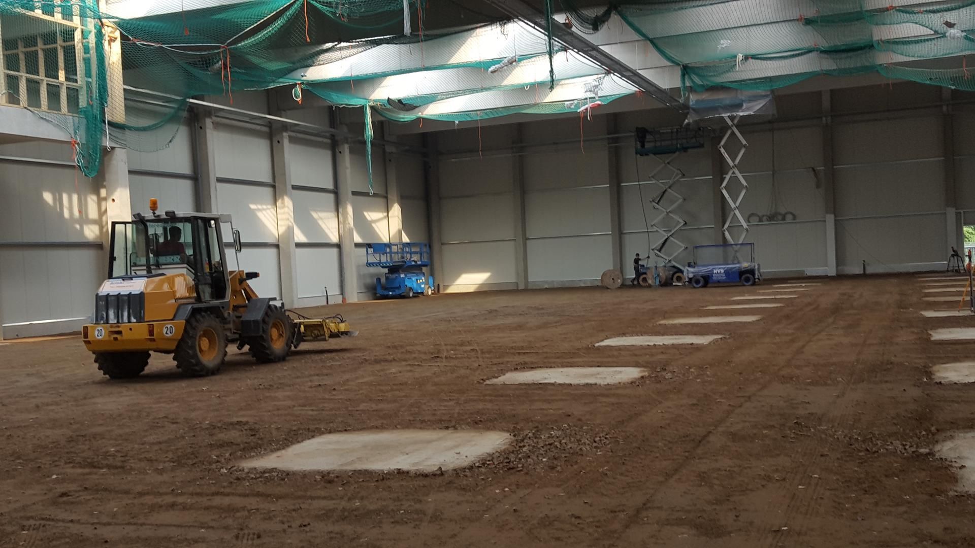 Ein gelber Traktor fährt durch eine große leere Lagerhalle.