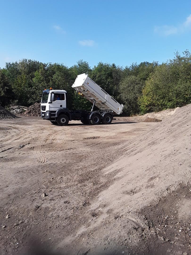 Ein Muldenkipper fährt eine unbefestigte Straße entlang eines Feldes.