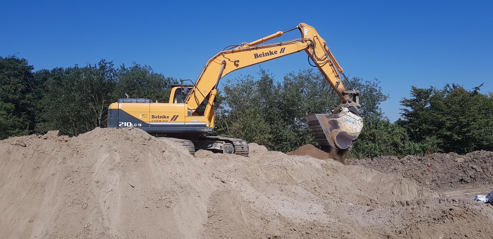 Ein gelber Bagger gräbt in einem Erdhaufen.