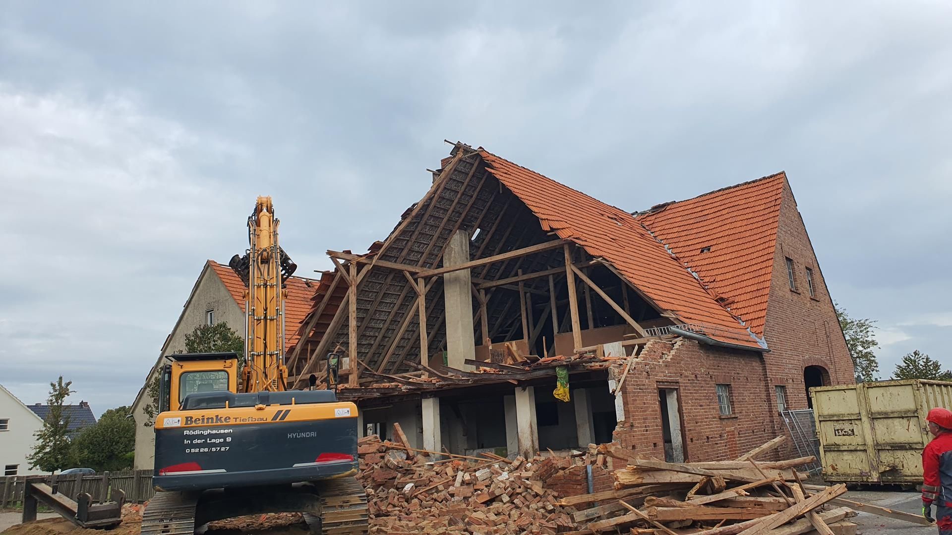 Ein großes Backsteinhaus wird von einem gelben Bagger abgerissen.