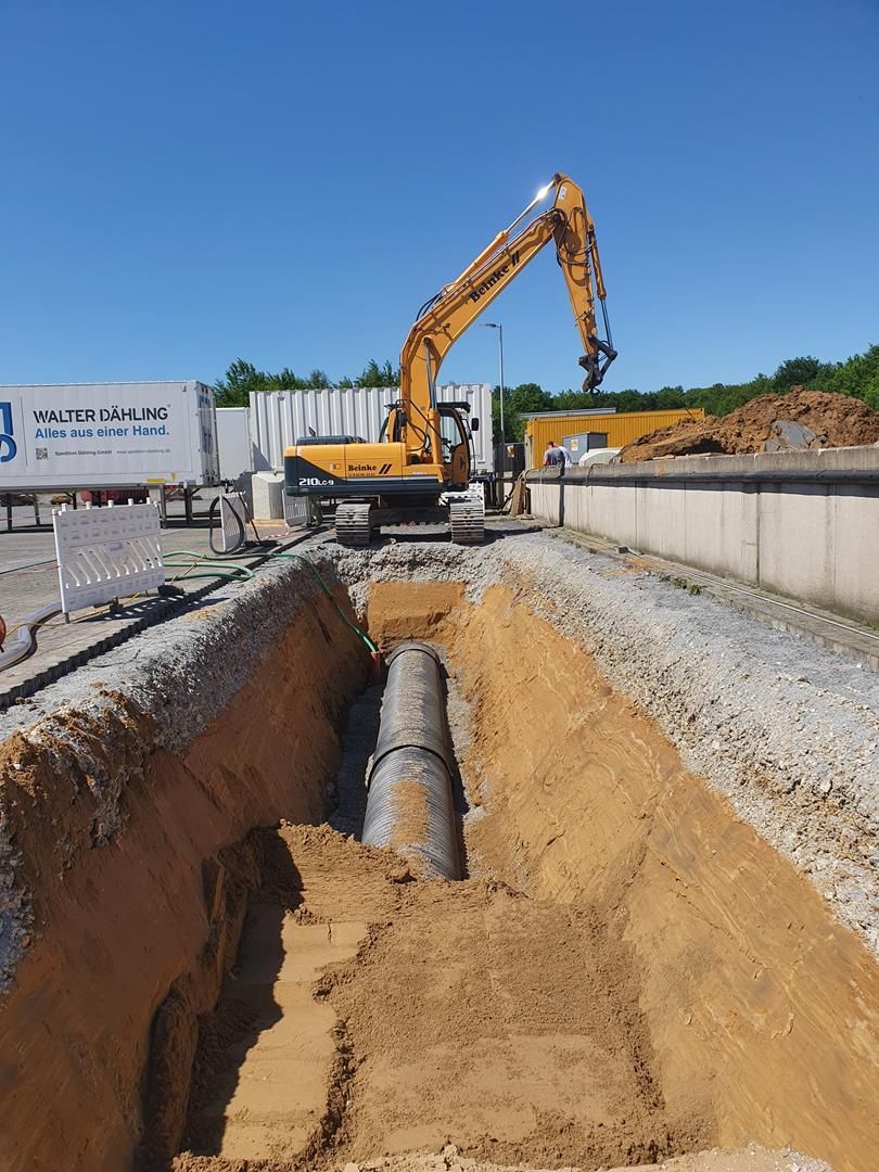 Ein gelber Bagger gräbt ein Loch in den Boden, um ein Rohr zu verlegen.