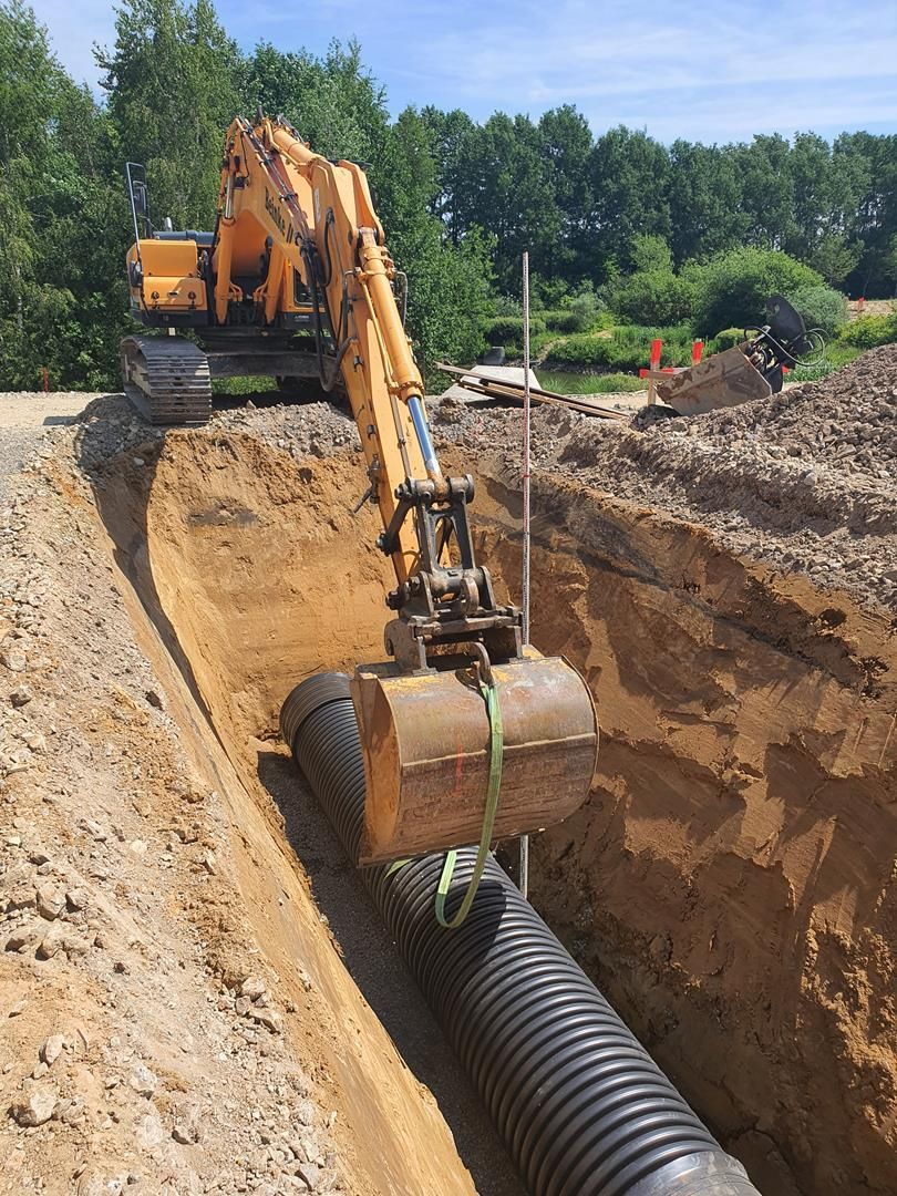 Ein gelber Bagger gräbt einen Graben neben einem schwarzen Rohr.