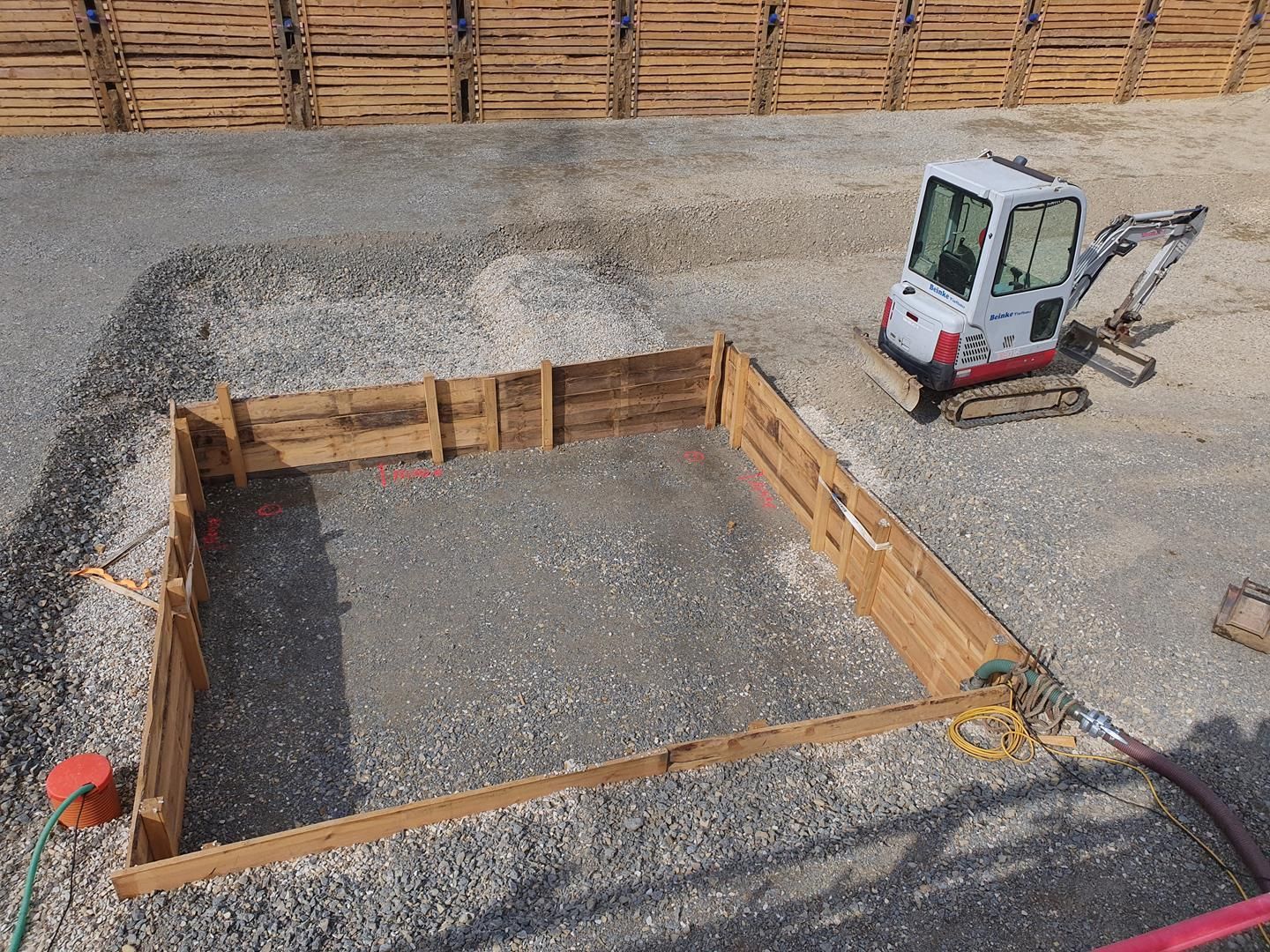 Ein kleiner Bagger steht auf einem Kieshaufen neben einem Holzzaun.