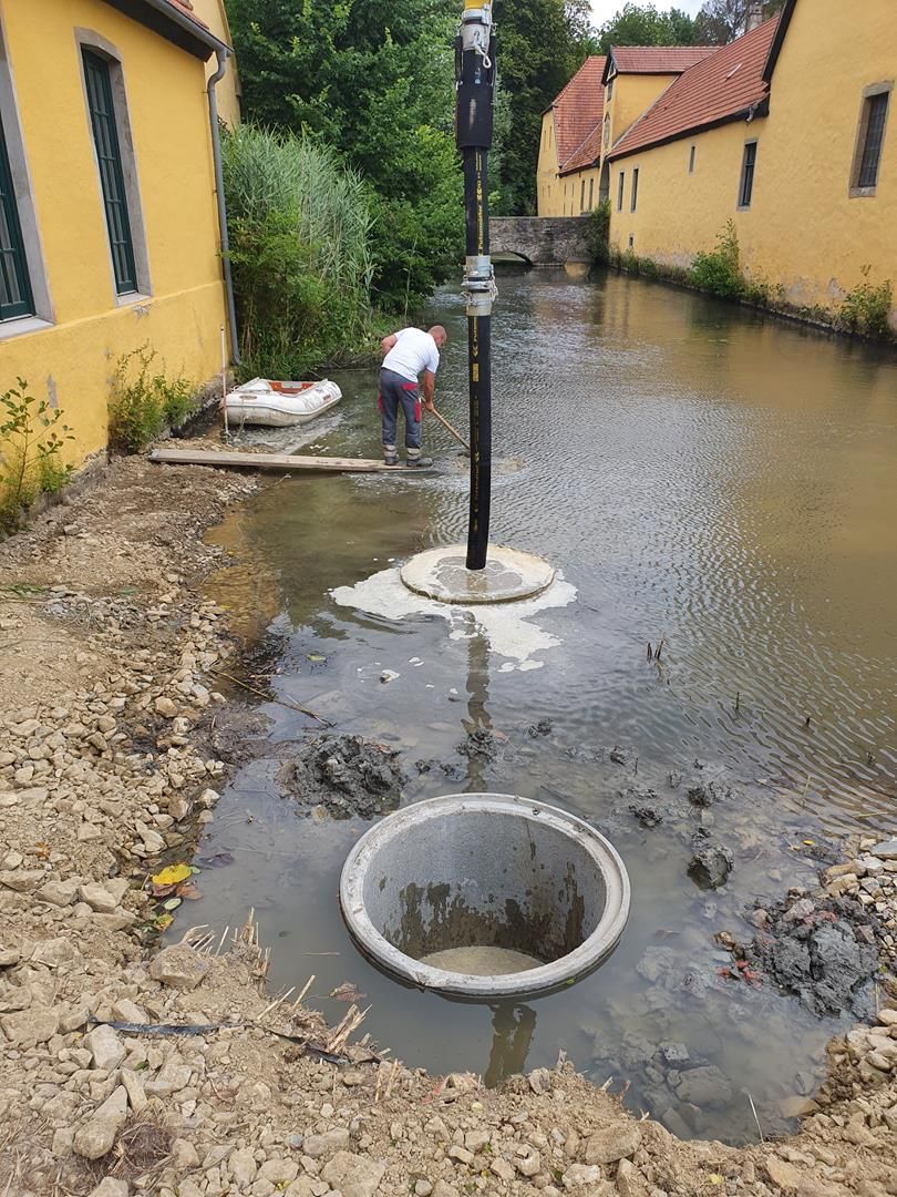 Ein Mann gräbt neben einem Gewässer ein Loch in den Boden.