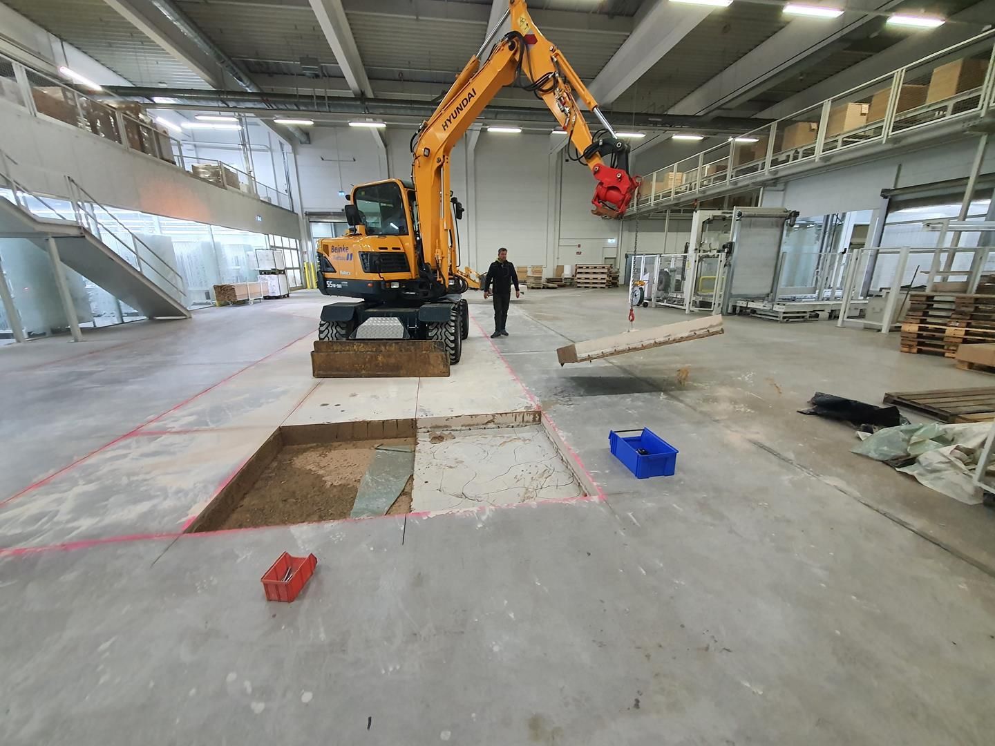 Ein Mann steht neben einem gelben Bagger in einer großen Lagerhalle.