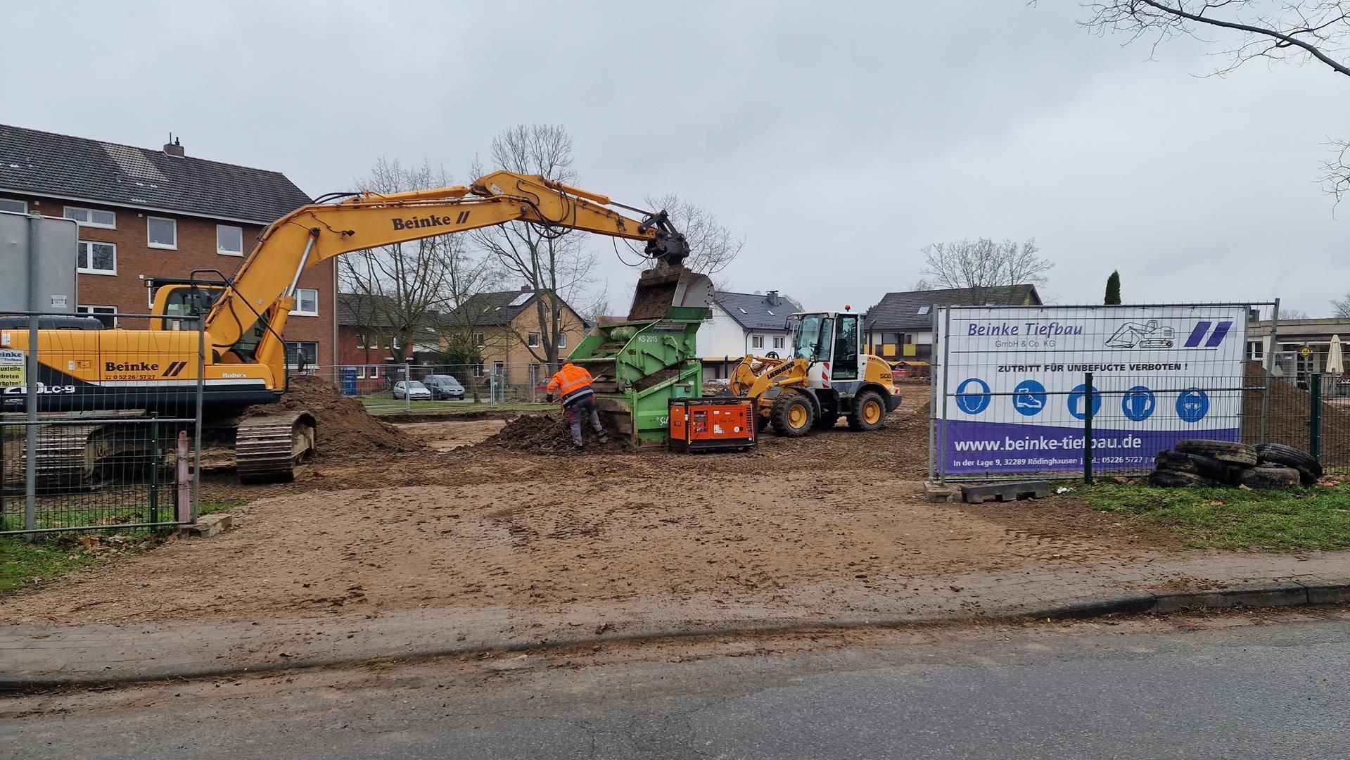 eine Baustelle mit vielen LKWs und einem großen Bagger.