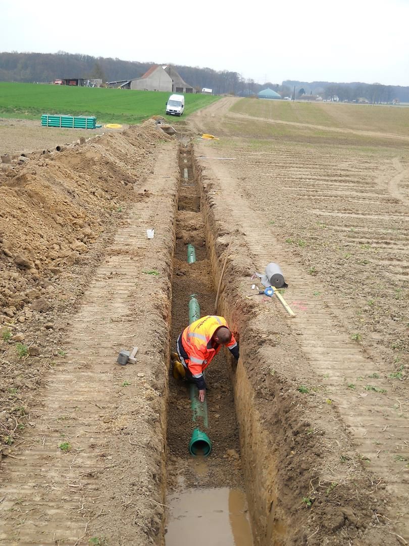 Ein Mann arbeitet an einem Rohr in einem Graben auf einem Feld.