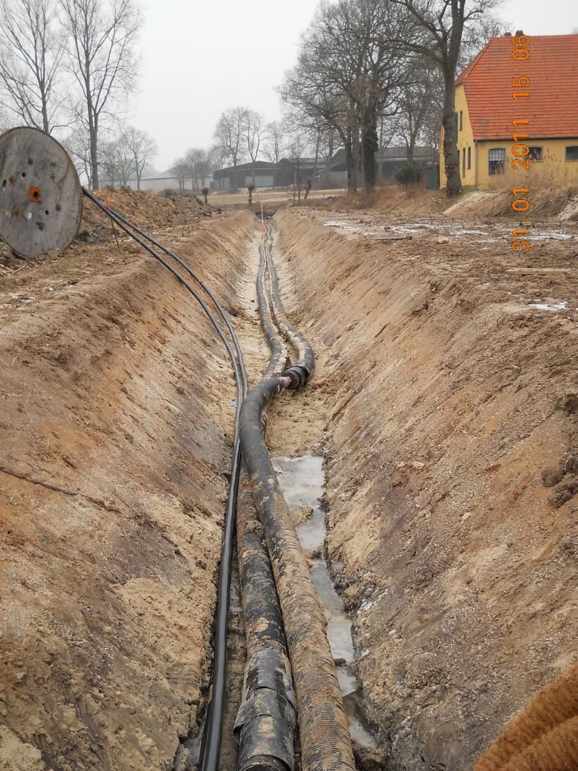 ein Graben mit vielen Rohren darin und ein Haus im Hintergrund.