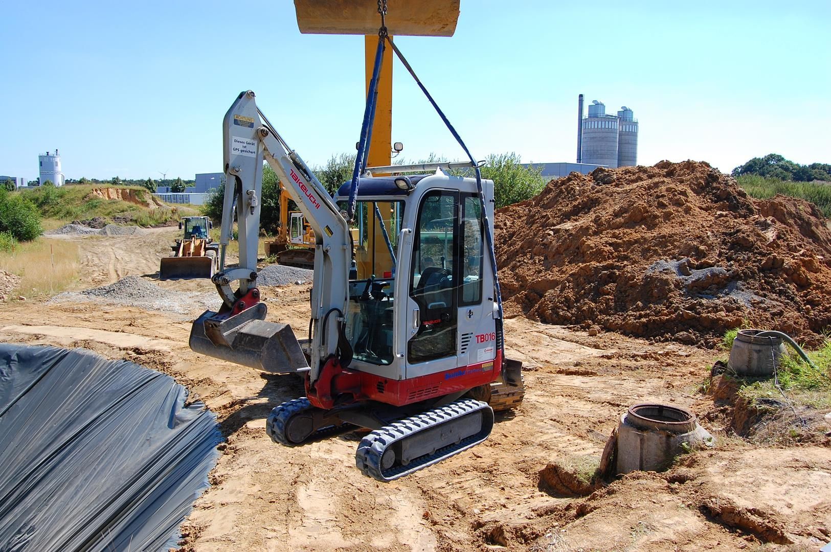Ein Bagger wird von einem Kran auf einer Baustelle angehoben.