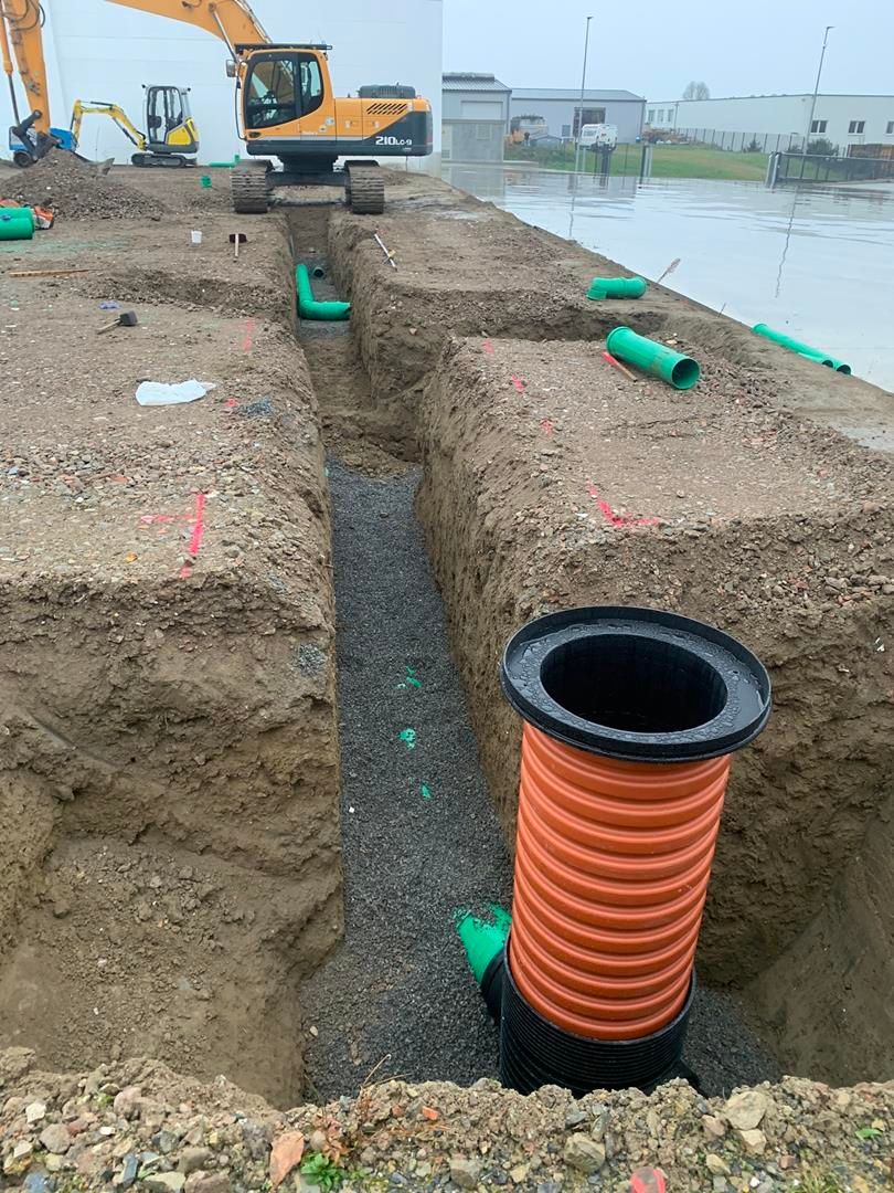 Ein großer Bagger gräbt neben einem großen Rohr ein Loch in den Boden.