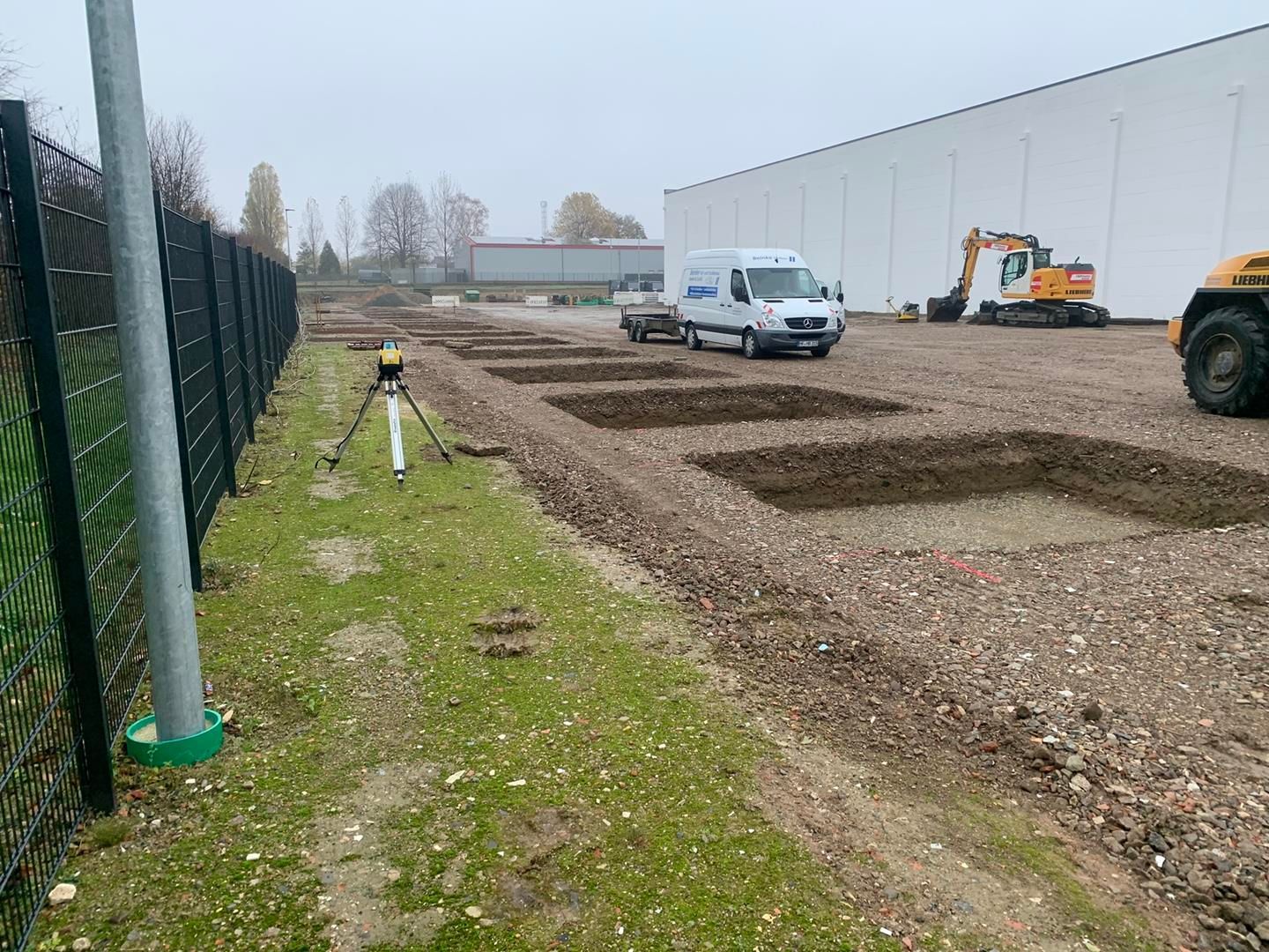 Ein weißer Lieferwagen parkt auf einem unbefestigten Parkplatz neben einem Zaun.