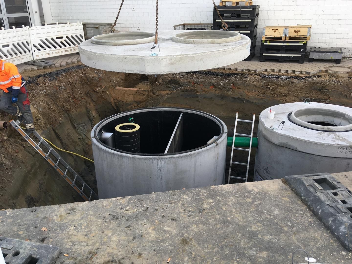 Ein Mann steht auf einer Leiter neben einem großen Betonzylinder in einem Loch.