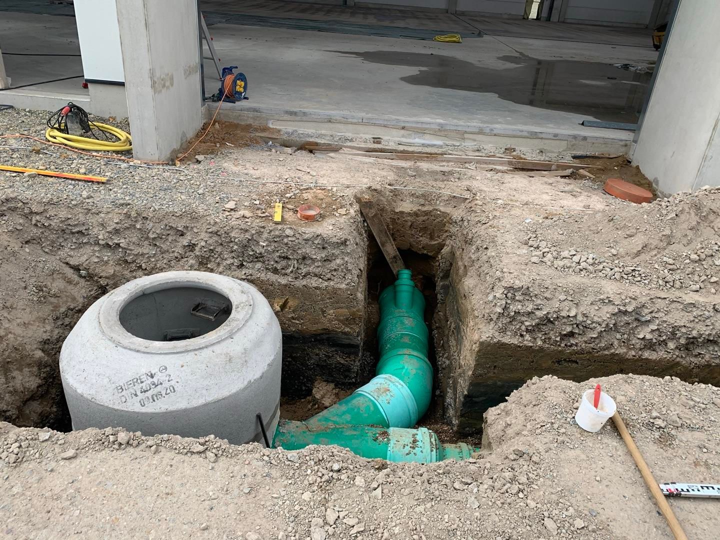 In einem Loch im Boden wird ein Abflussrohr verlegt.