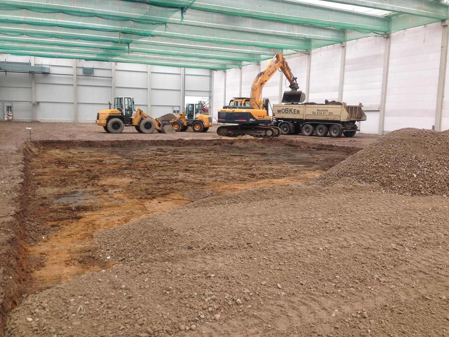 Ein Muldenkipper wird in einer großen Lagerhalle mit Erde beladen.