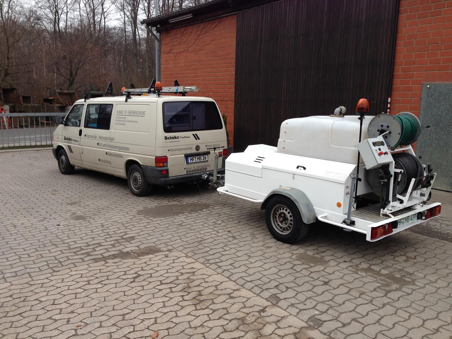 Ein Lieferwagen mit daran befestigtem Anhänger parkt vor einem Gebäude.