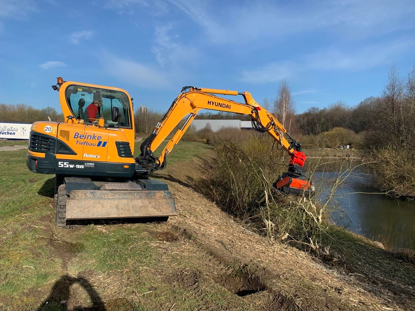 Ein gelber Bagger arbeitet an einem Flussufer.
