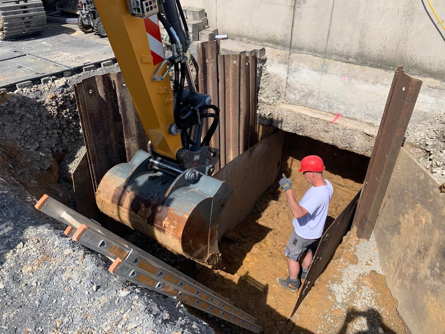 Ein Mann steht in einem Loch neben einem Baufahrzeug.