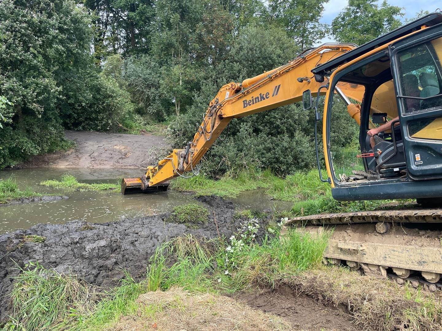 Ein großer gelber Bagger gräbt ein Loch in den Schlamm.