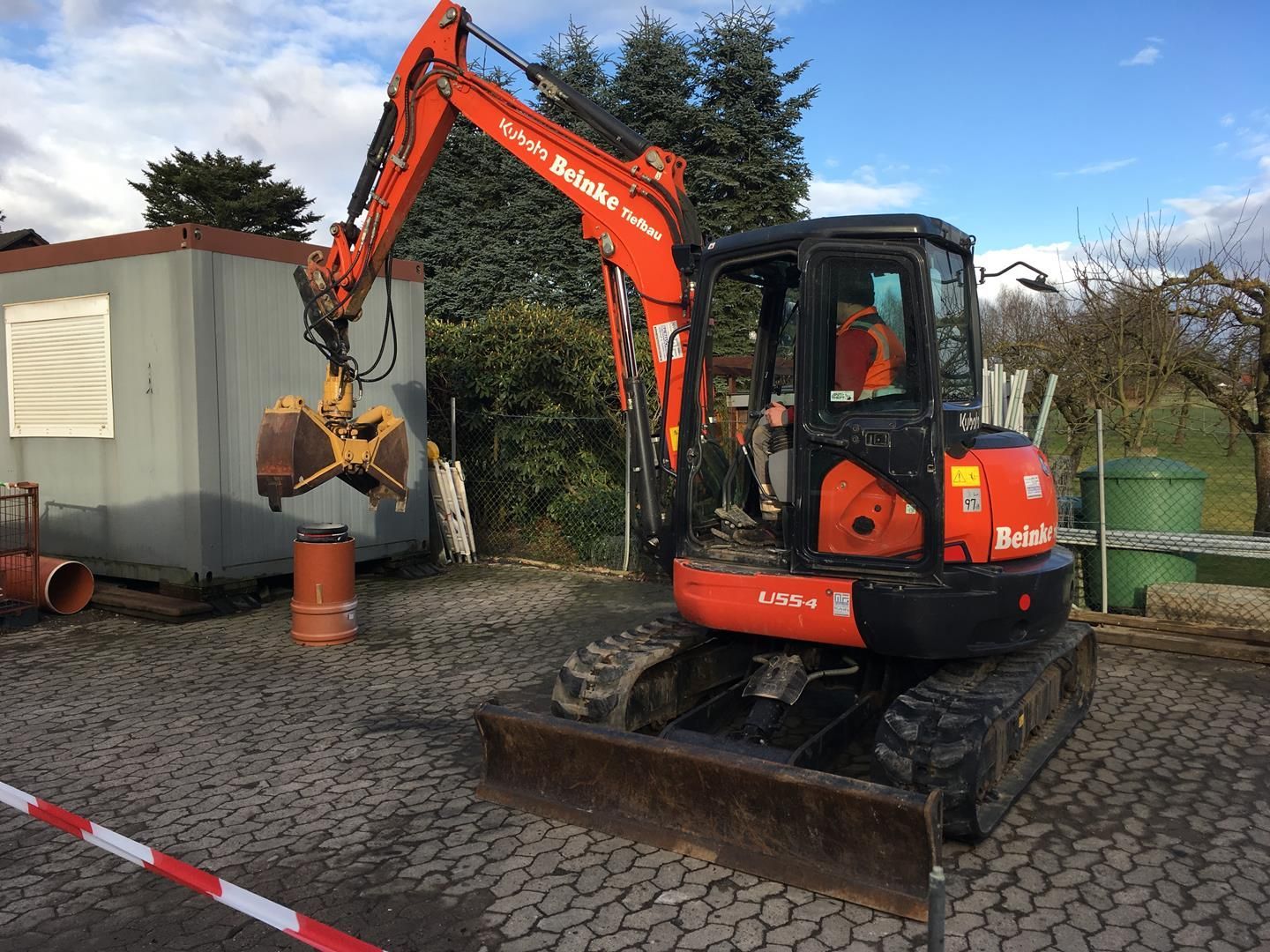 Ein Mann fährt einen orangefarbenen Bagger auf einem Parkplatz.