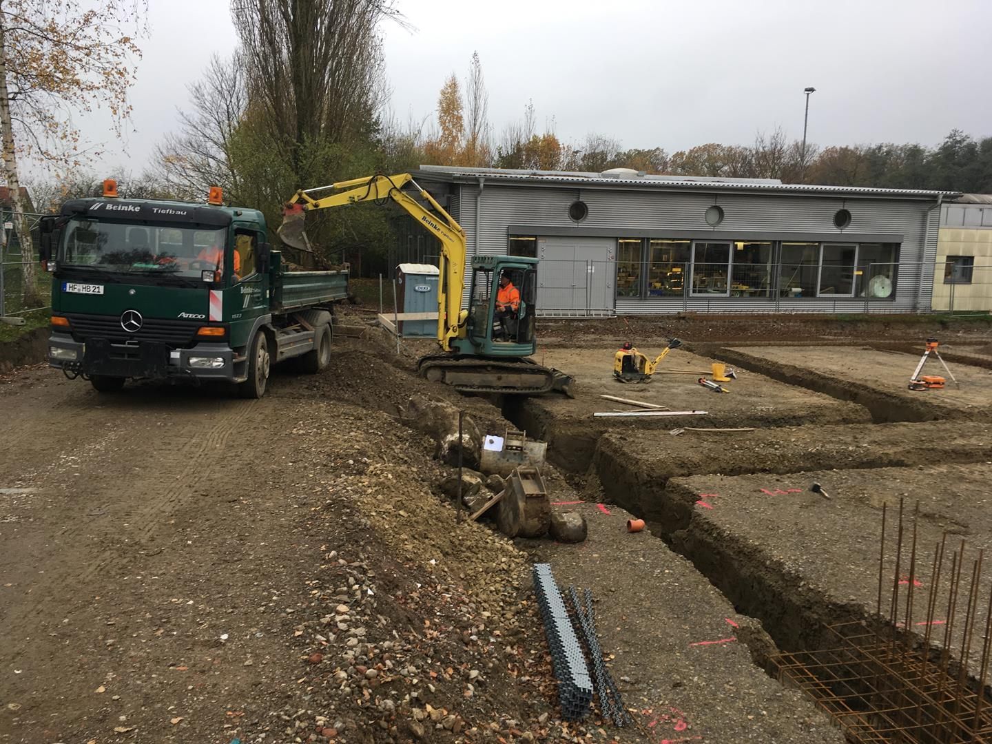 Eine Baustelle mit einem LKW und einem Bagger vor einem Gebäude.