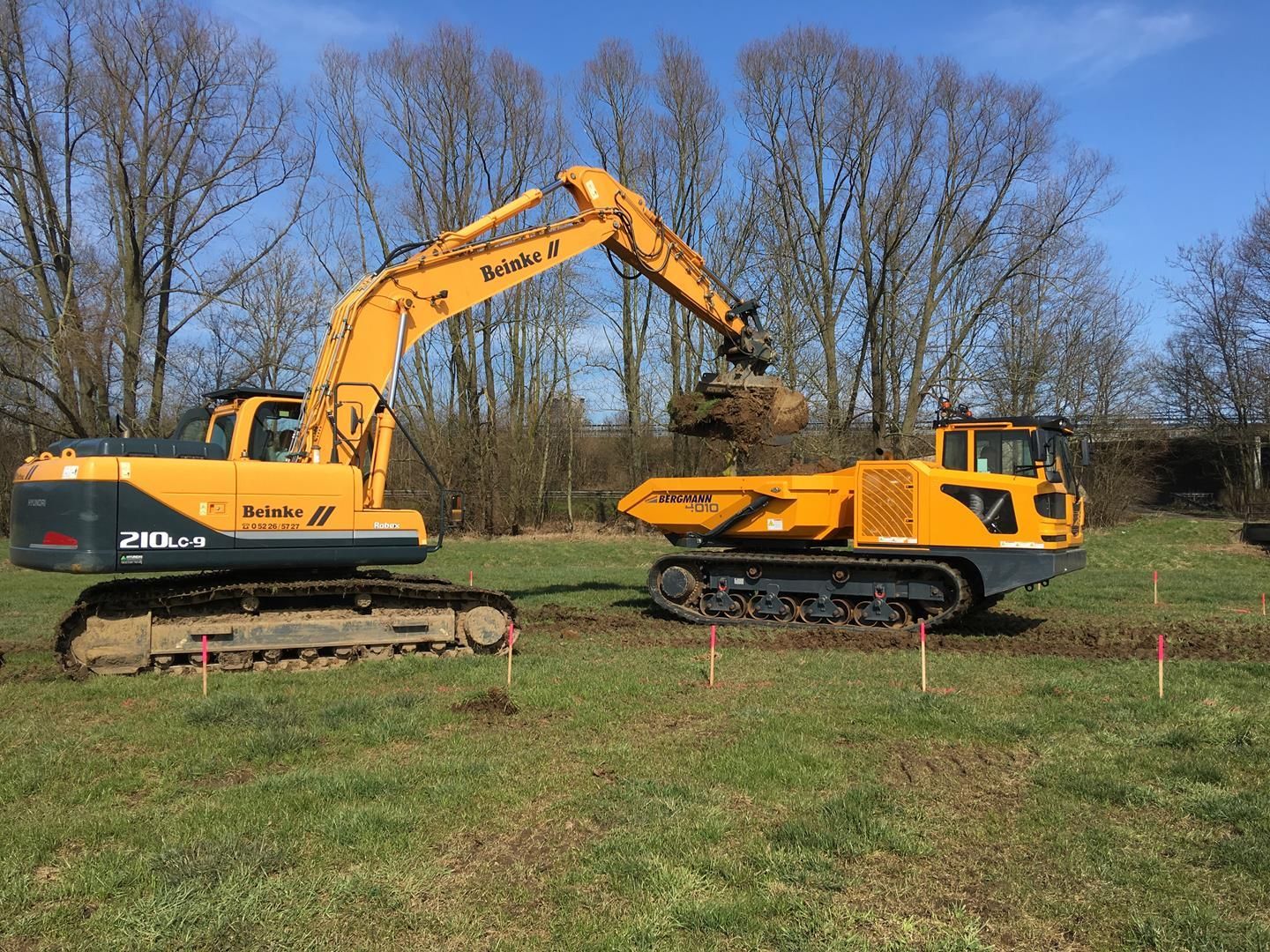Ein gelber Bagger gräbt ein Loch in einem Feld neben einem Muldenkipper.