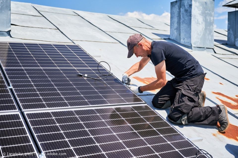 Mann installiert Solarpaneele auf einem Dach.