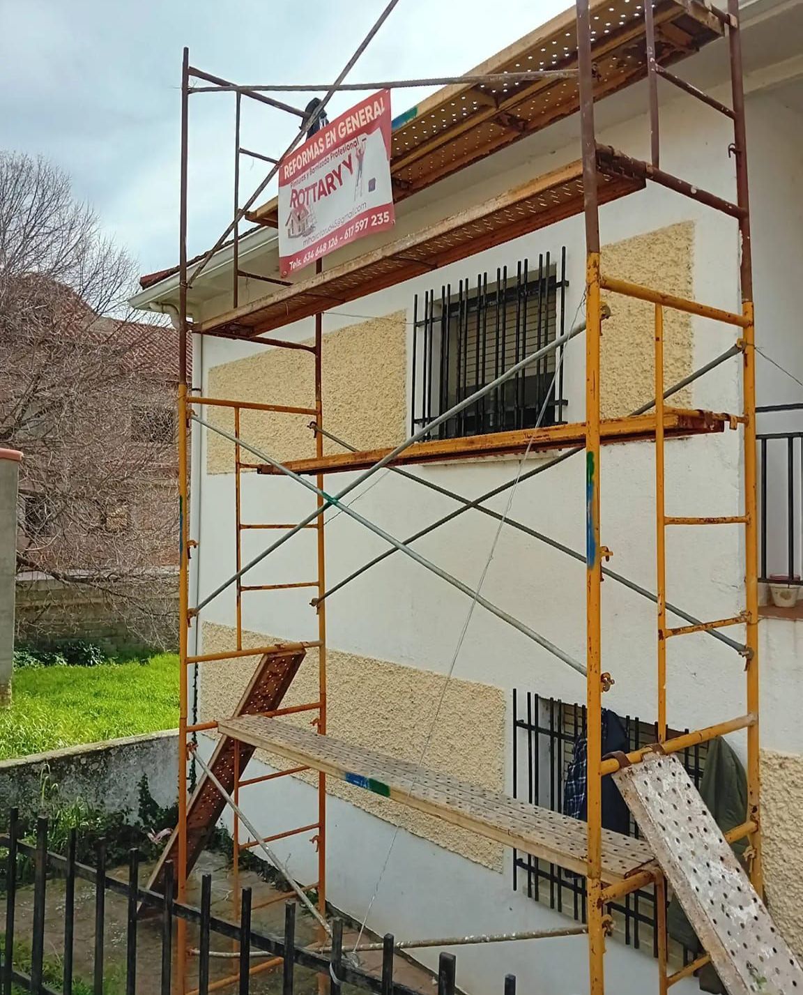 Un andamio amarillo está situado delante de un edificio blanco.