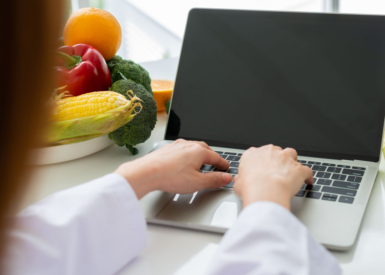 Nutricionista presenta datos dietéticos en una tableta, con verduras frescas y una computadora portátil en el escritorio.