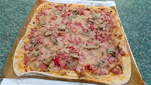 Sobre una mesa hay una pizza con jamón, champiñones y queso.
