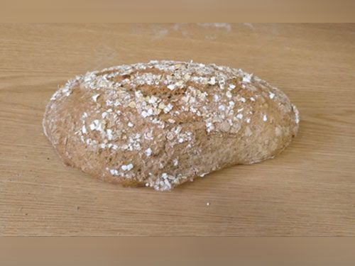 Una hogaza de pan con avena encima está sobre una mesa de madera.