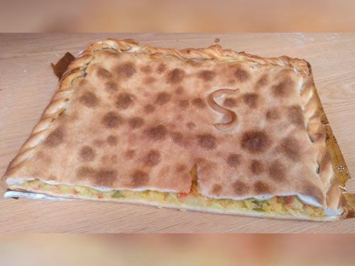 Una pizza con la letra s tallada está sobre una mesa de madera.