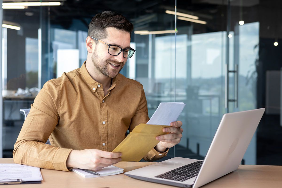 Homme qui ouvre une lettre devant son ordinateur
