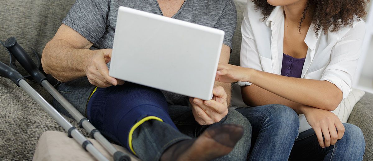 Infirmière qui aide un homme en béquille sur l'ordinateur