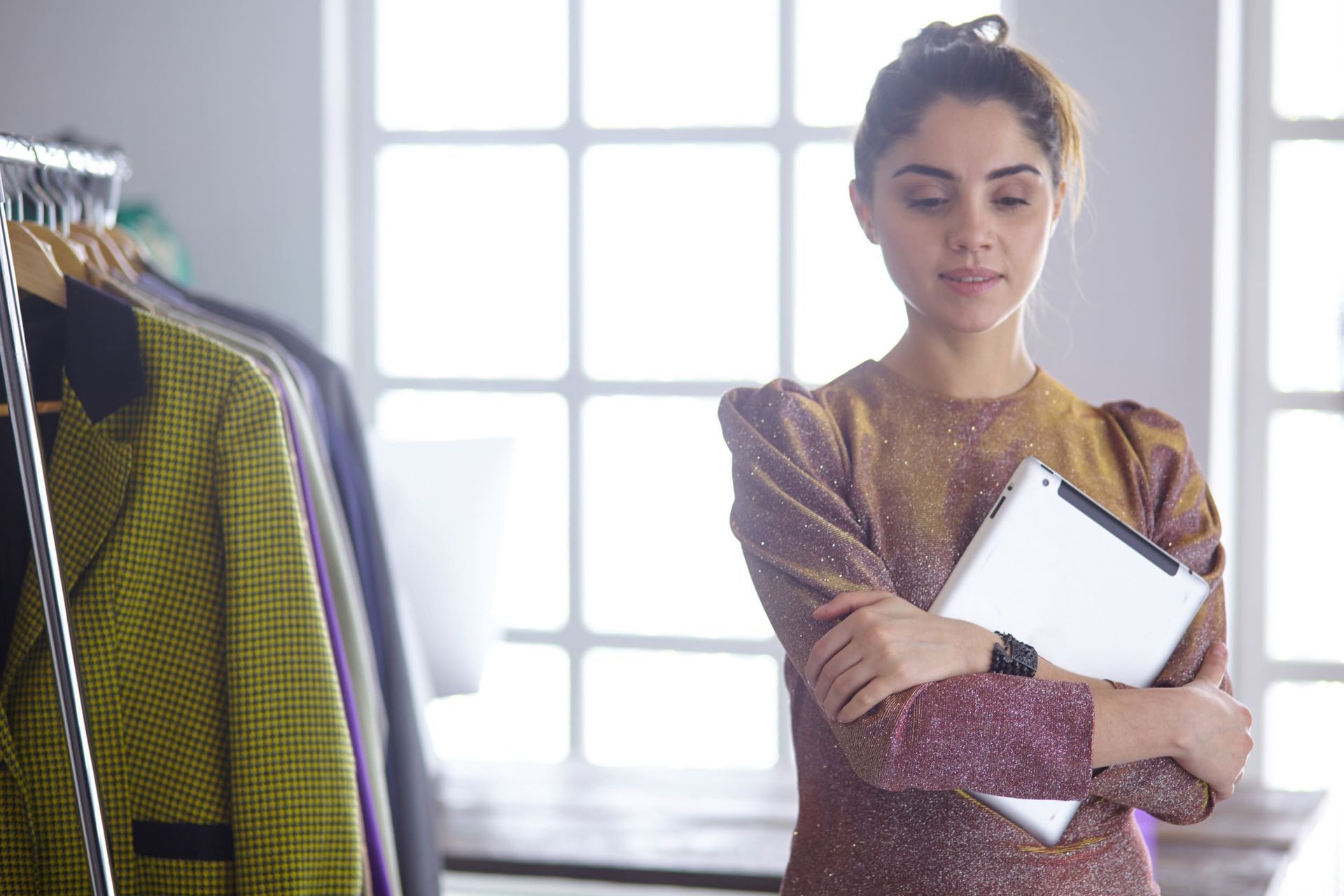 Una mujer está parada frente a un perchero con ropa sosteniendo una tableta.