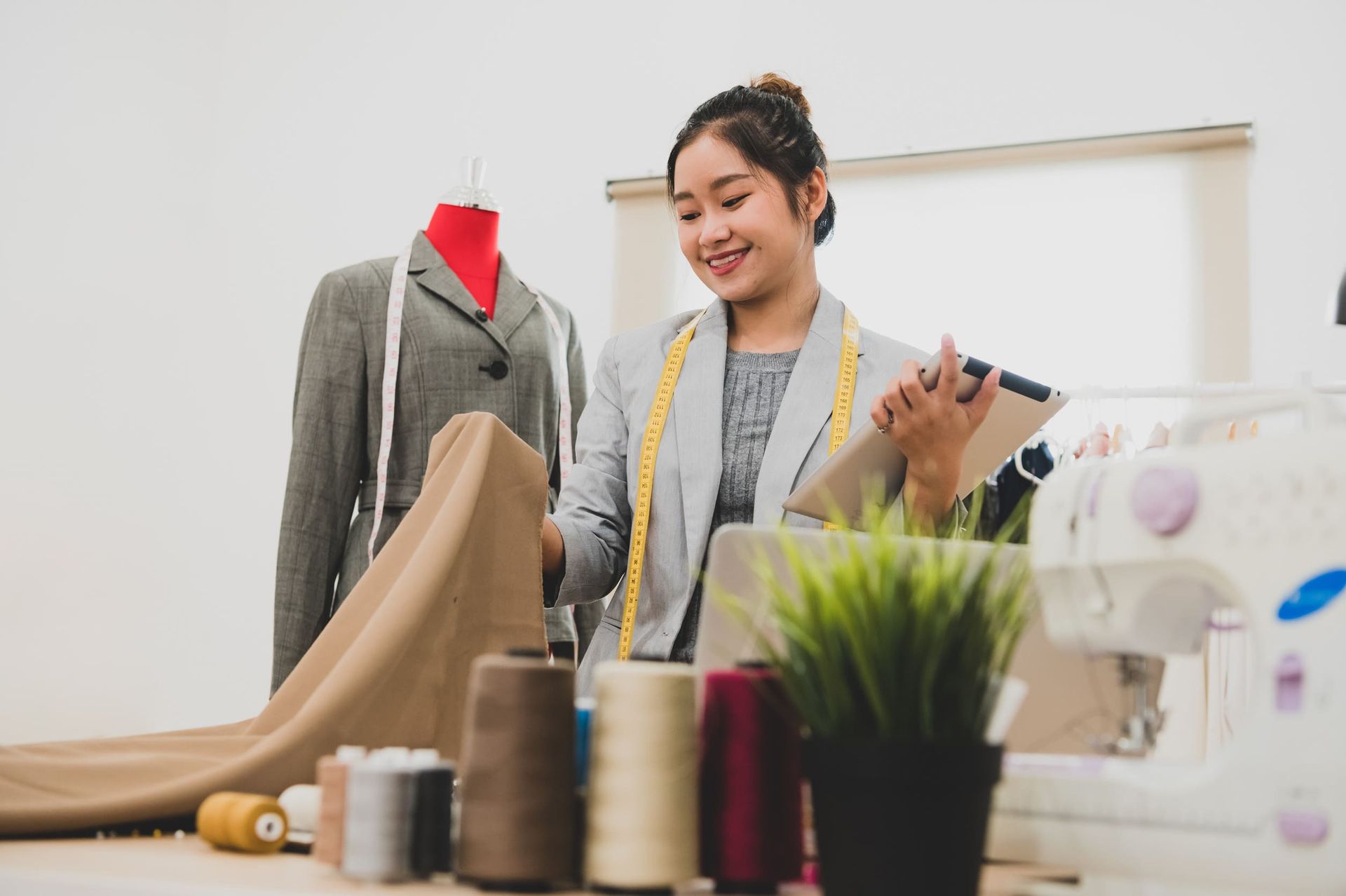 Una mujer está parada frente a una máquina de coser sosteniendo un trozo de tela.
