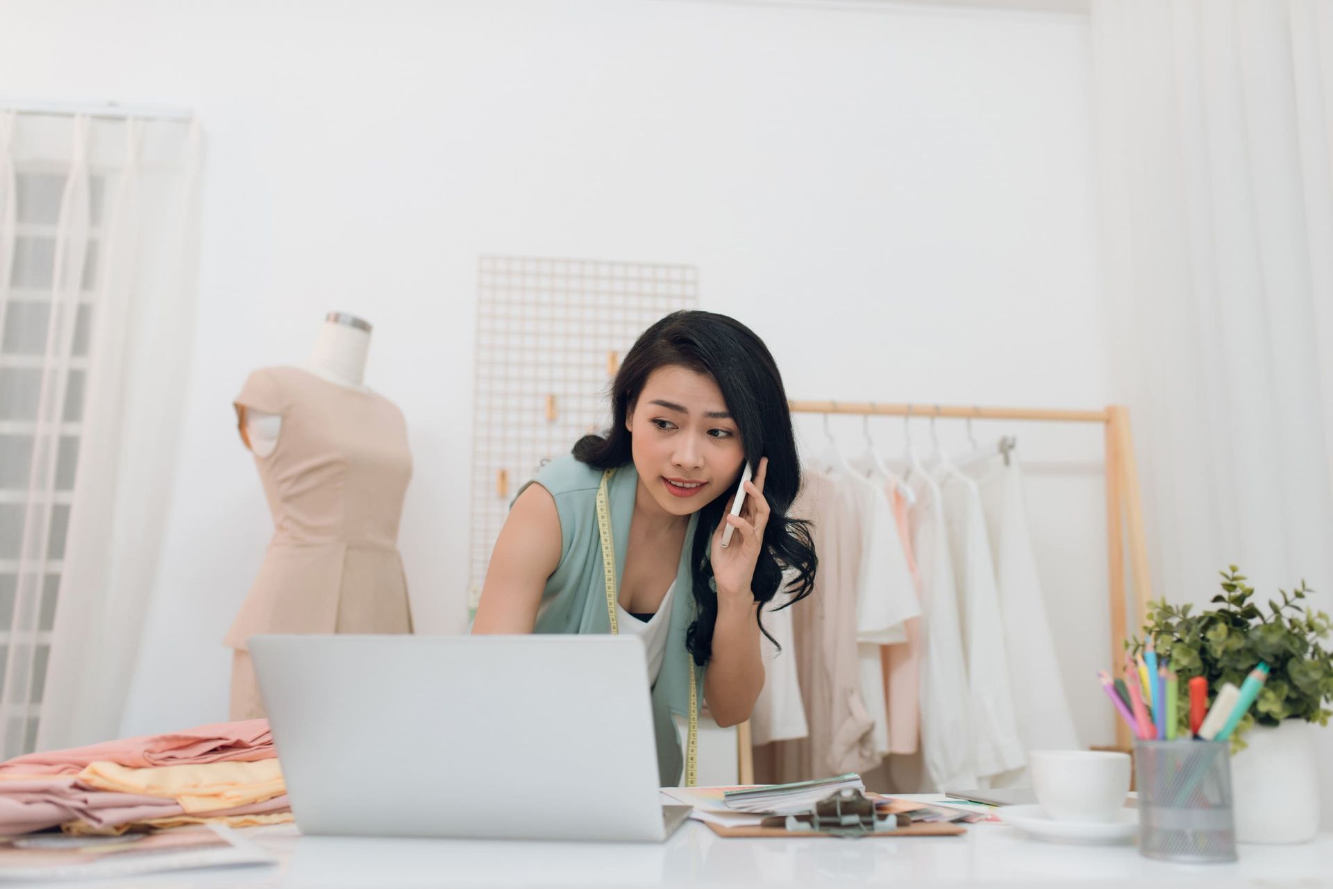 Una mujer está sentada en un escritorio con una computadora portátil y hablando por un teléfono celular.