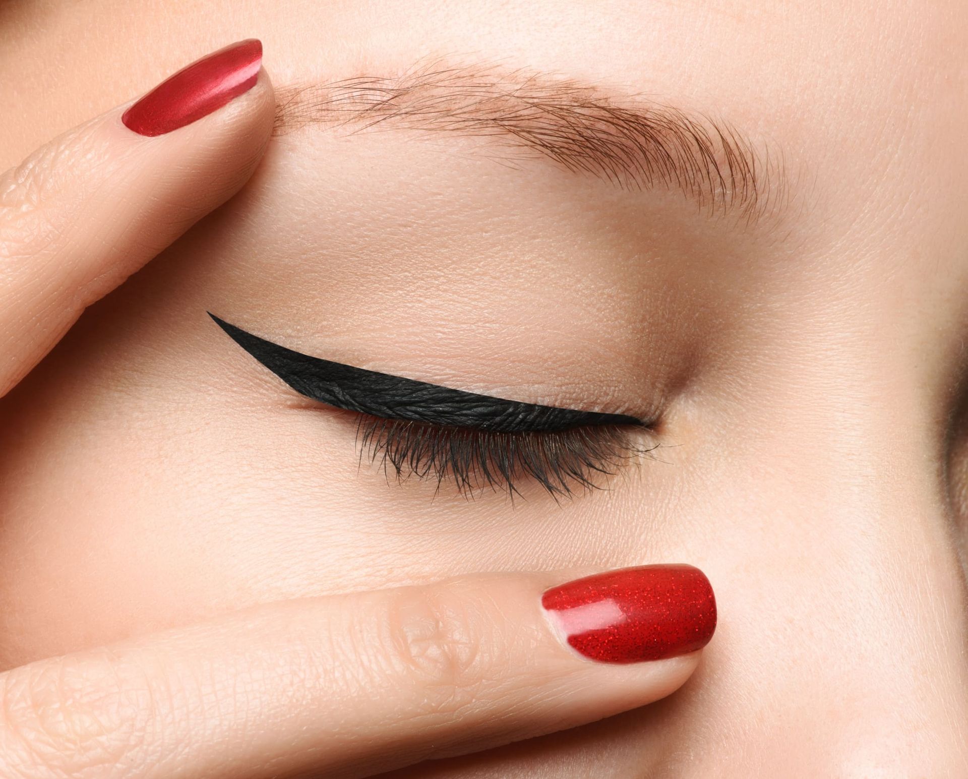 Una mujer con uñas rojas se aplica delineador de ojos.