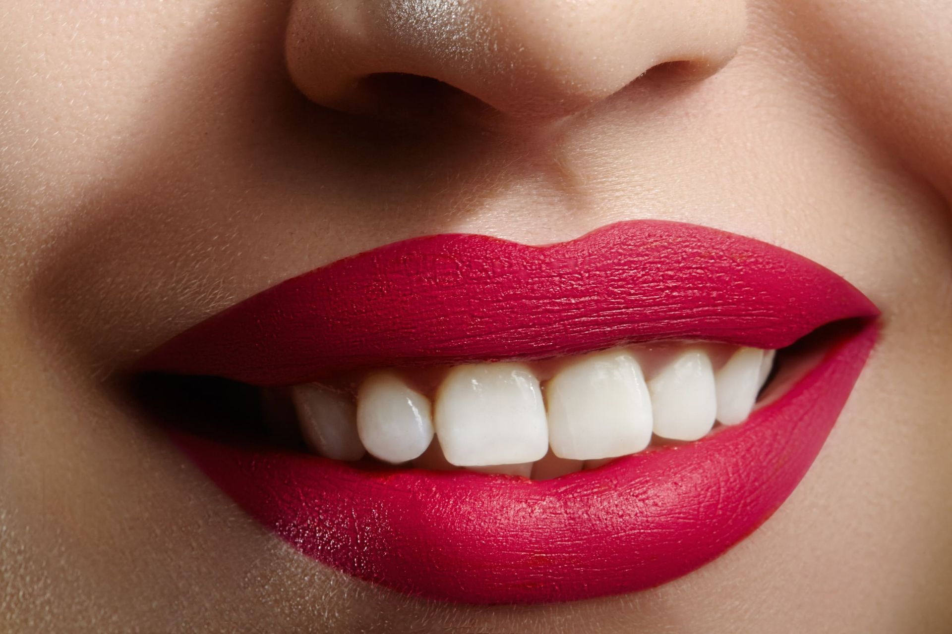 Un primer plano de la boca de una mujer con lápiz labial rojo y dientes blancos.