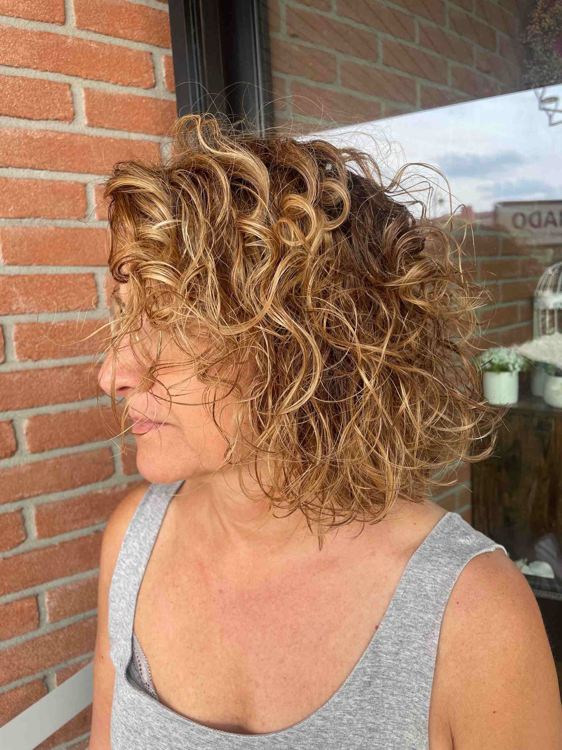 Donna con capelli biondi ricci, che indossa una canottiera grigia.