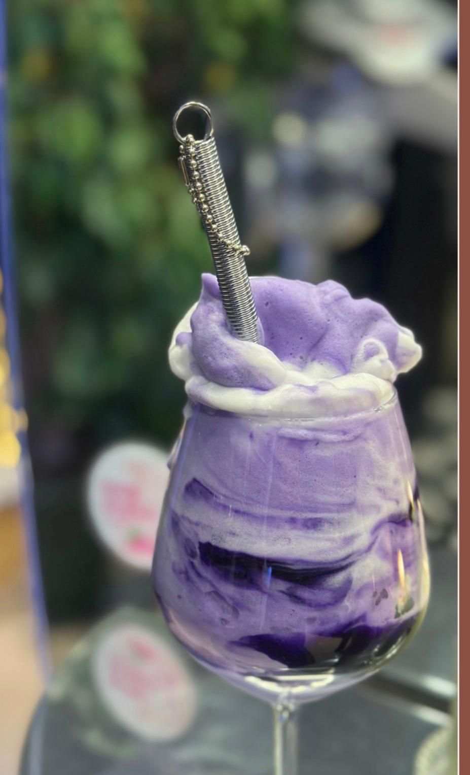 Dessert viola in un bicchiere con stelo, guarnito con una pallina di panna montata viola e un cucchiaio.