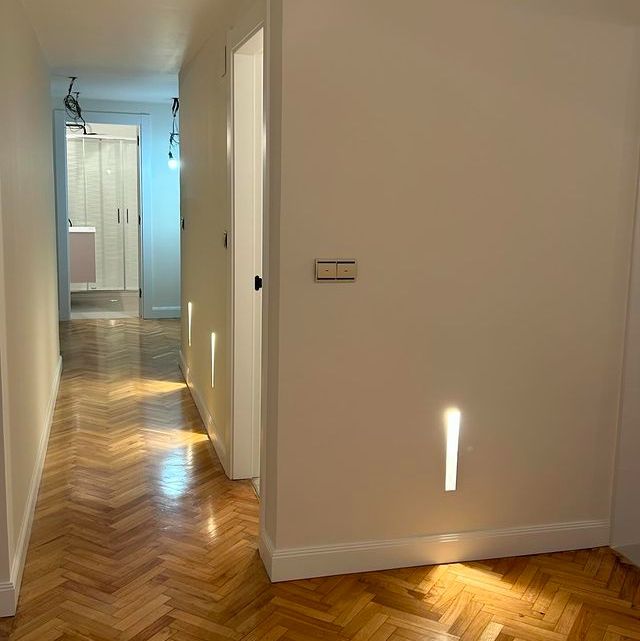 Un pasillo con suelo de madera y una luz en la pared.