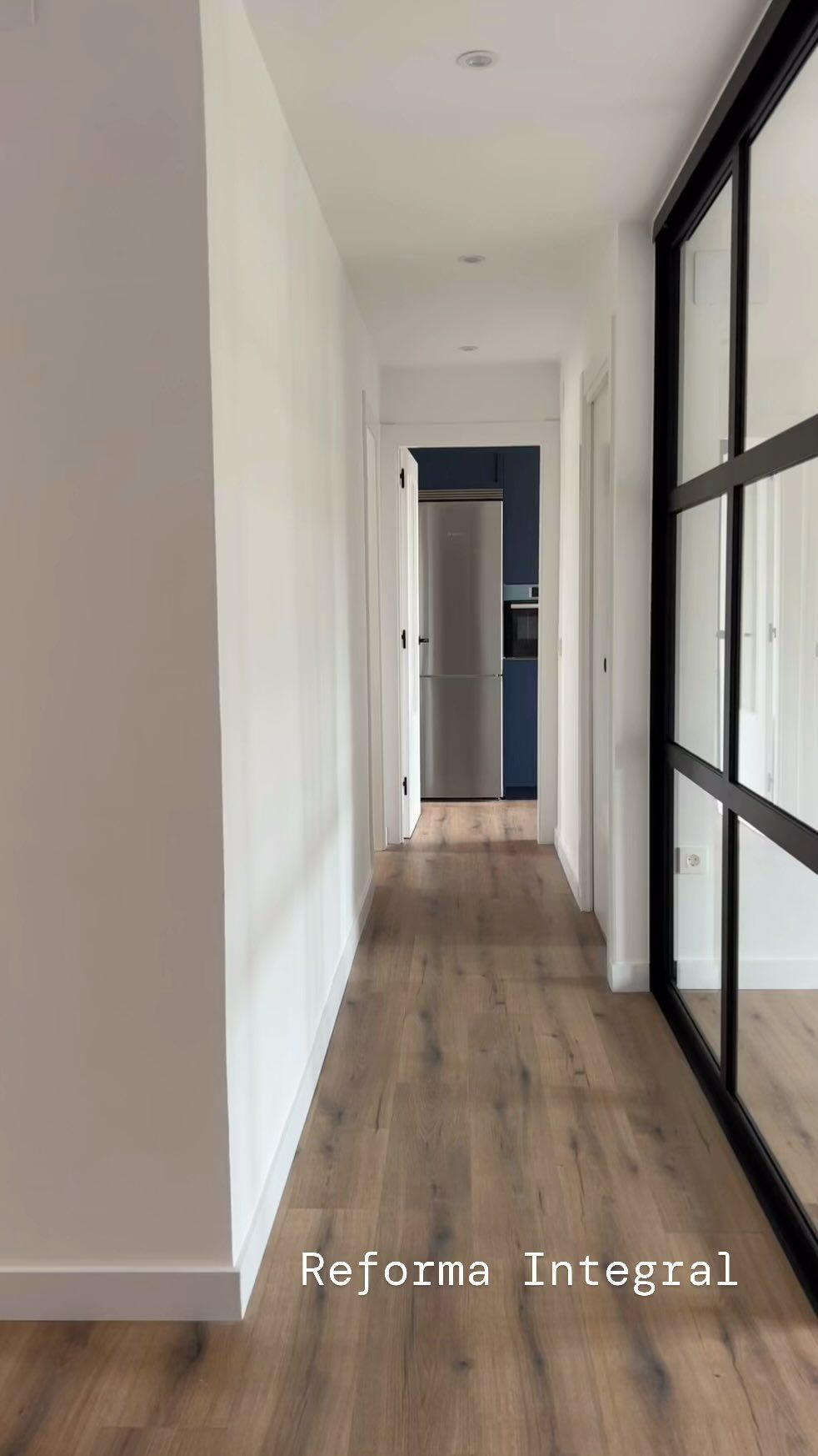 Un largo pasillo con pisos de madera y puertas corredizas de vidrio que conducen a una cocina.