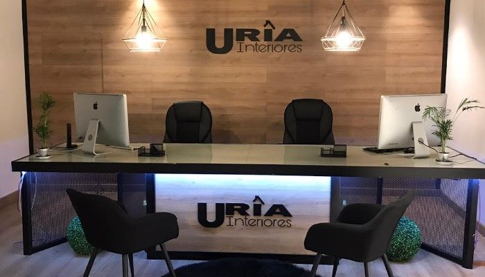 Un área de recepción con un escritorio y sillas y un cartel que dice Uria Interiores.