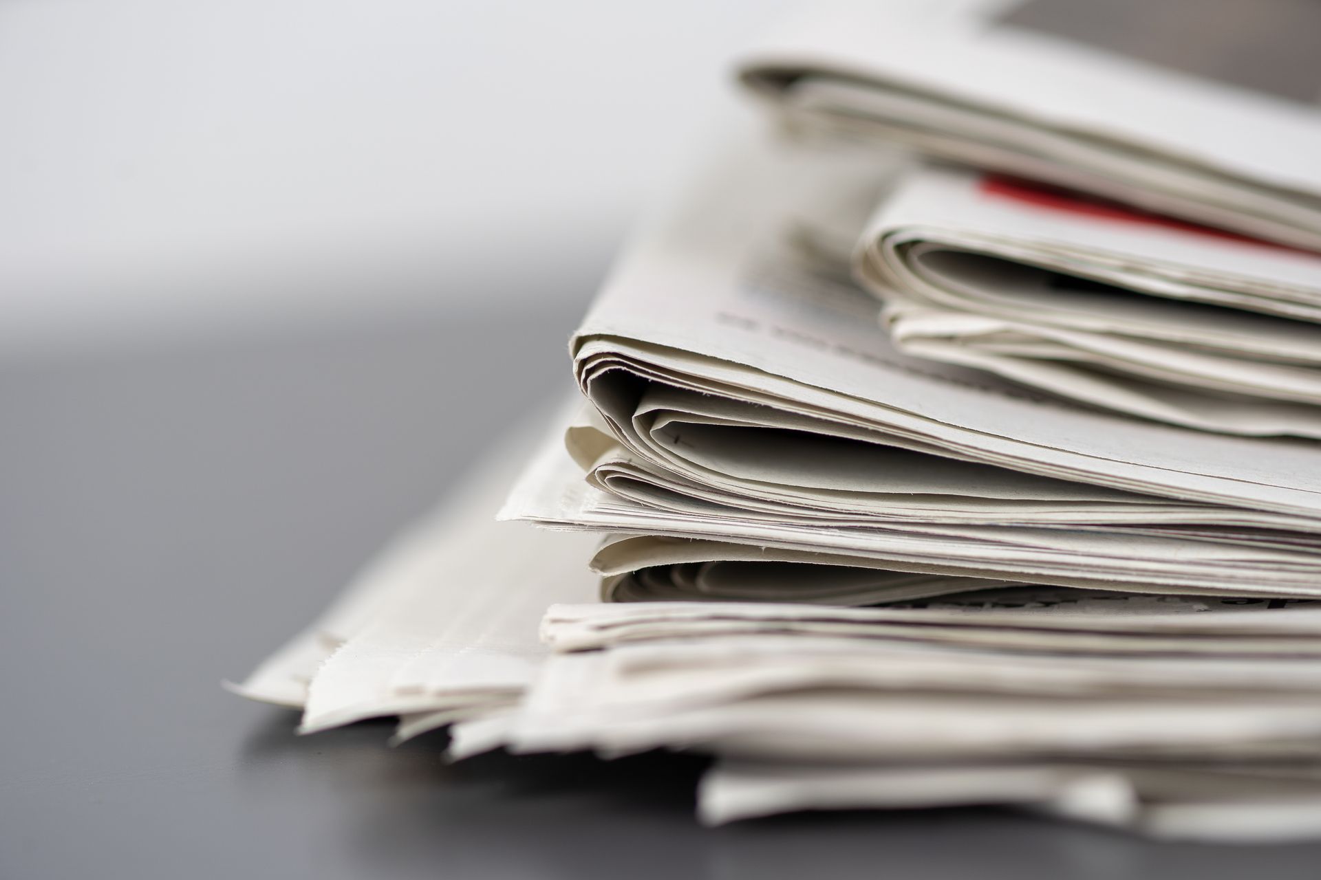 Pile de journaux ou de magazines pliés sur une table, laissant apparaître des pages blanches et rouges.