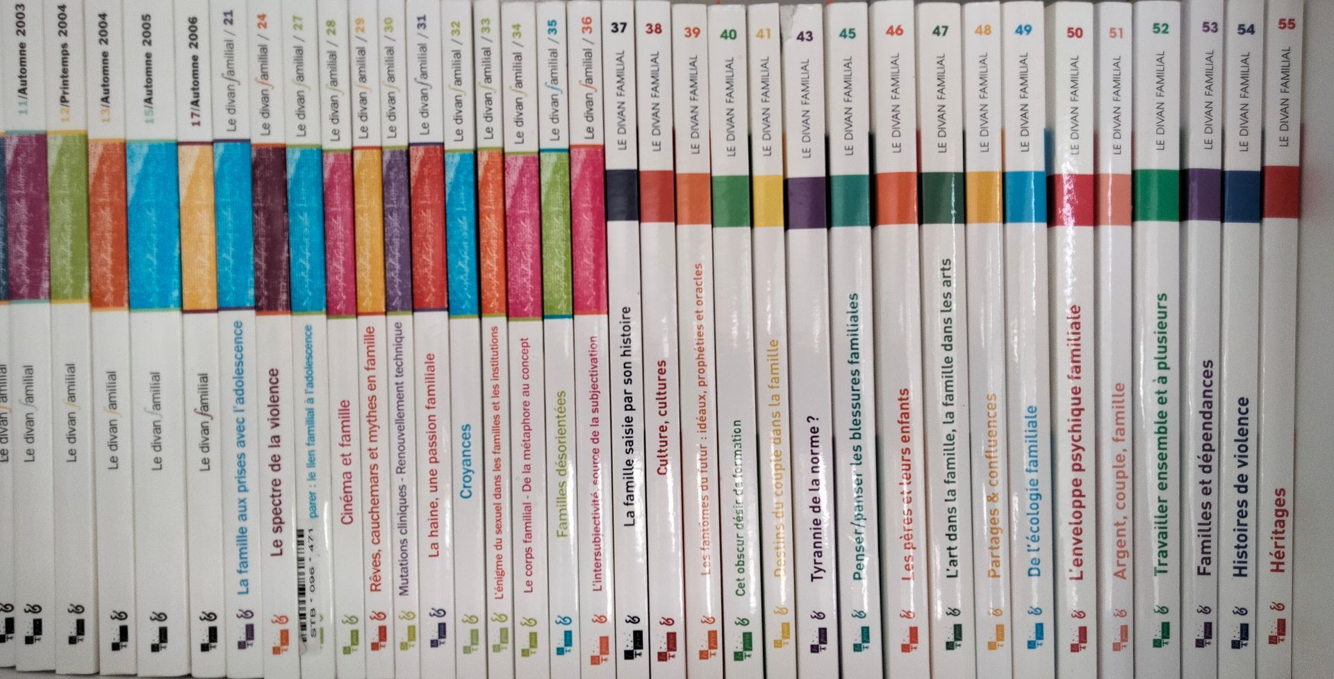 Rangée de tranches de livres colorées disposées sur une étagère sur fond blanc.