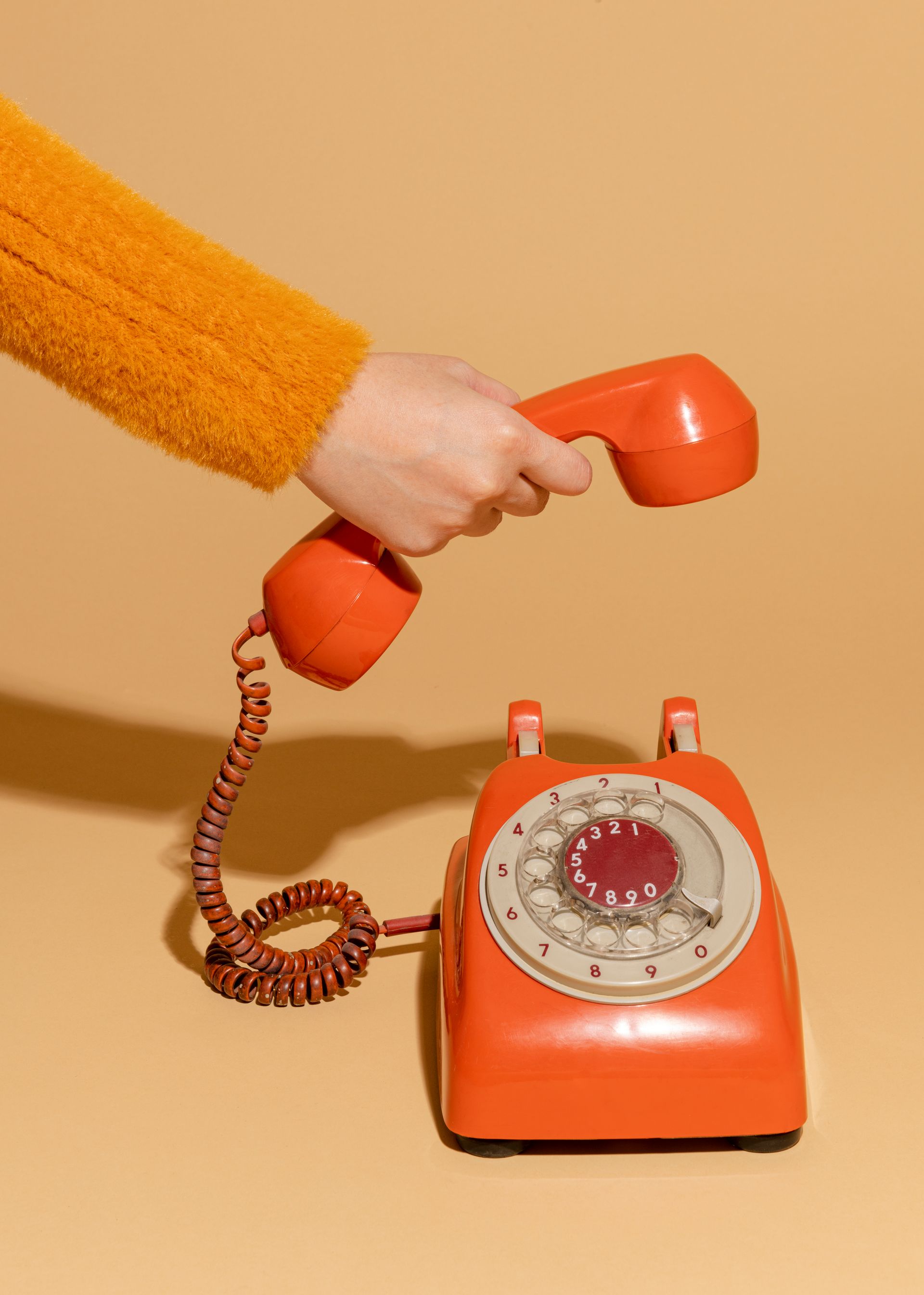 Main tenant un combiné téléphonique à cadran orange au-dessus d'un téléphone orange assorti sur fond beige