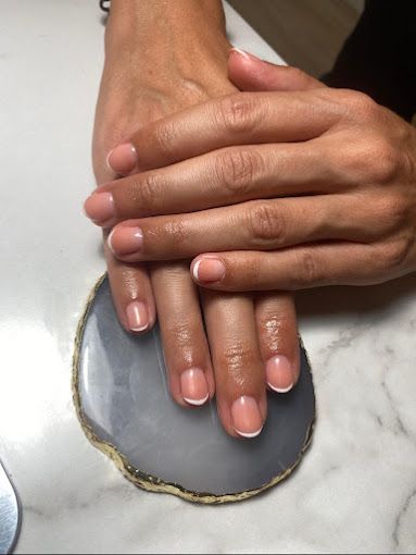 Un primer plano de las manos de una mujer con manicura francesa sobre una mesa.