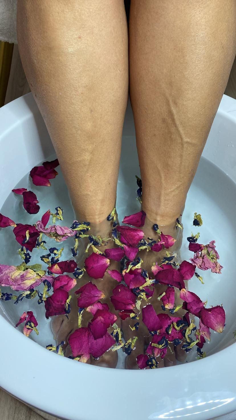 Una mujer está sentada en un recipiente con agua con pétalos en sus pies.